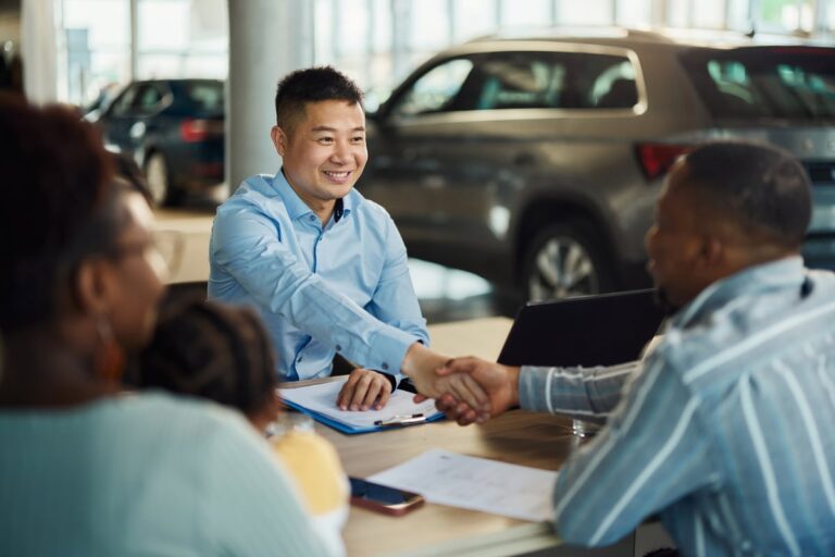 Salesman and customer shaking hands over paperwork at car dealership 7KT2UtX