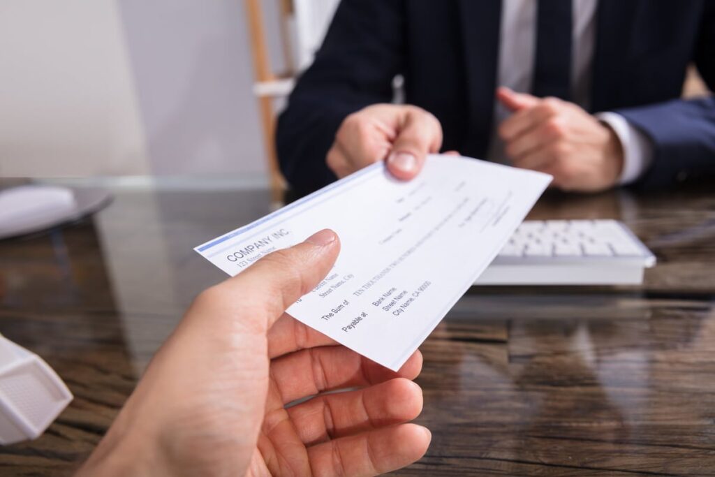 man in suit handing over a paycheck GettyImages 928077630 hDmsZKb