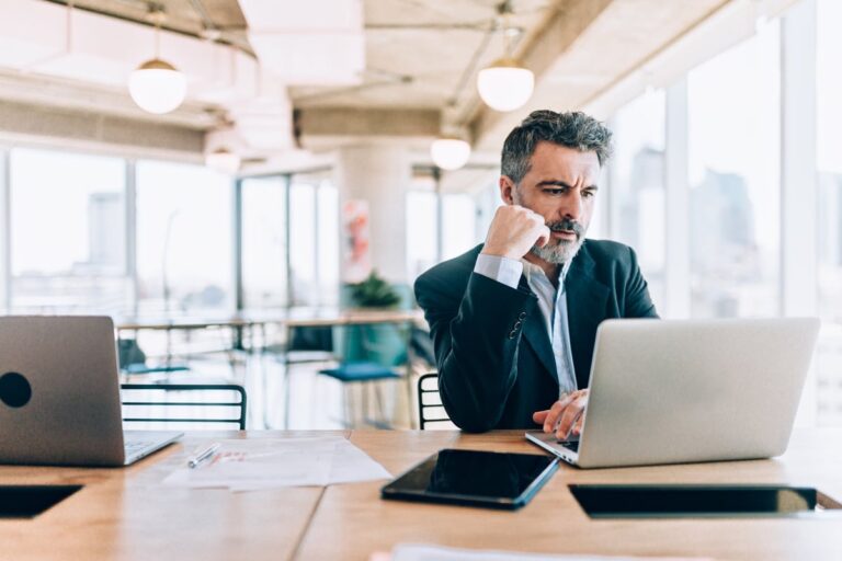 Mature man with tablet and laptop appearing worried zJbNIZD