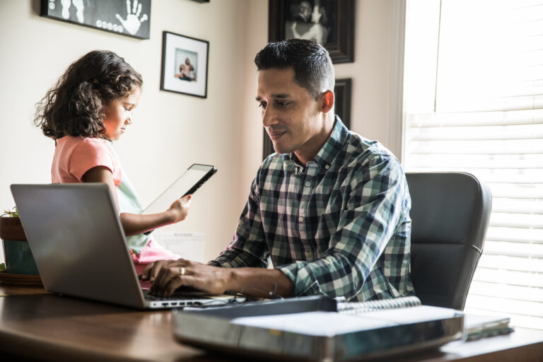 person sitting at a desk looking at a laptop with a child nearby