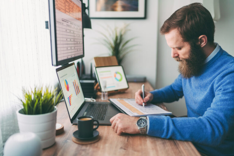 bearded person at desk by computer taking notes