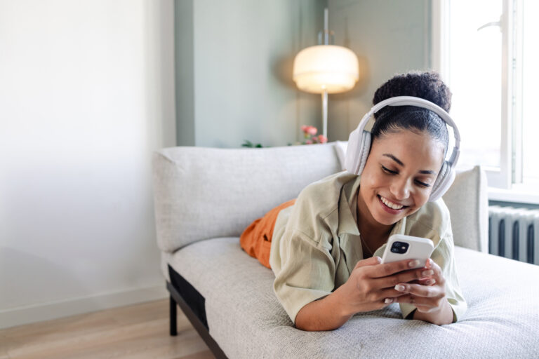 happy person using headphones and a phone while lying on a couch