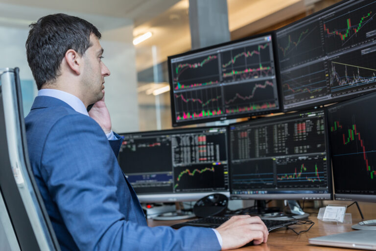 person in front of multiple computer screens looking at stock graphs