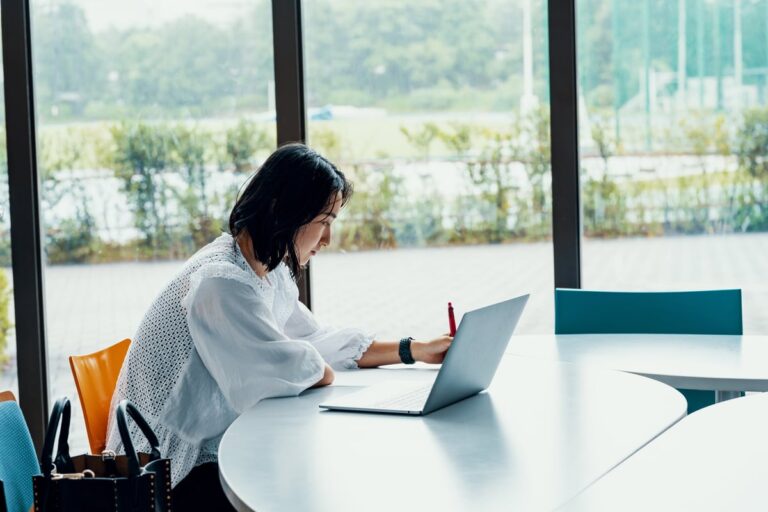 person writing at desk next to laptop D1Jgf3k