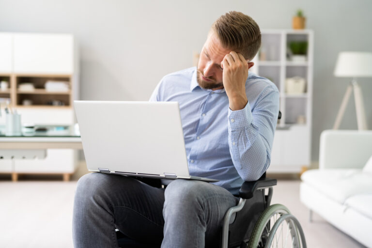 person in wheelchair looking unhappy while wielding a laptop