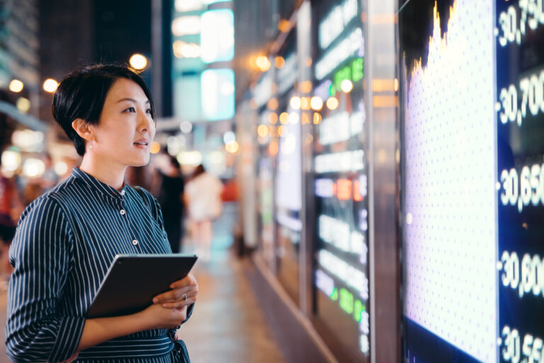 a person holds a tablet and looks at a stock chart and price movements on a city street